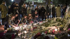 epa05025819 People pray, place flowers and light candles in tribute for the victims of the 13 November Paris attacks near the Bataclan concert venue in Paris, France, 14 November 2015. At least 129 people were killed in a series of attacks in Paris on 13 November, according to French officials. EPA/IAN LANGSDON